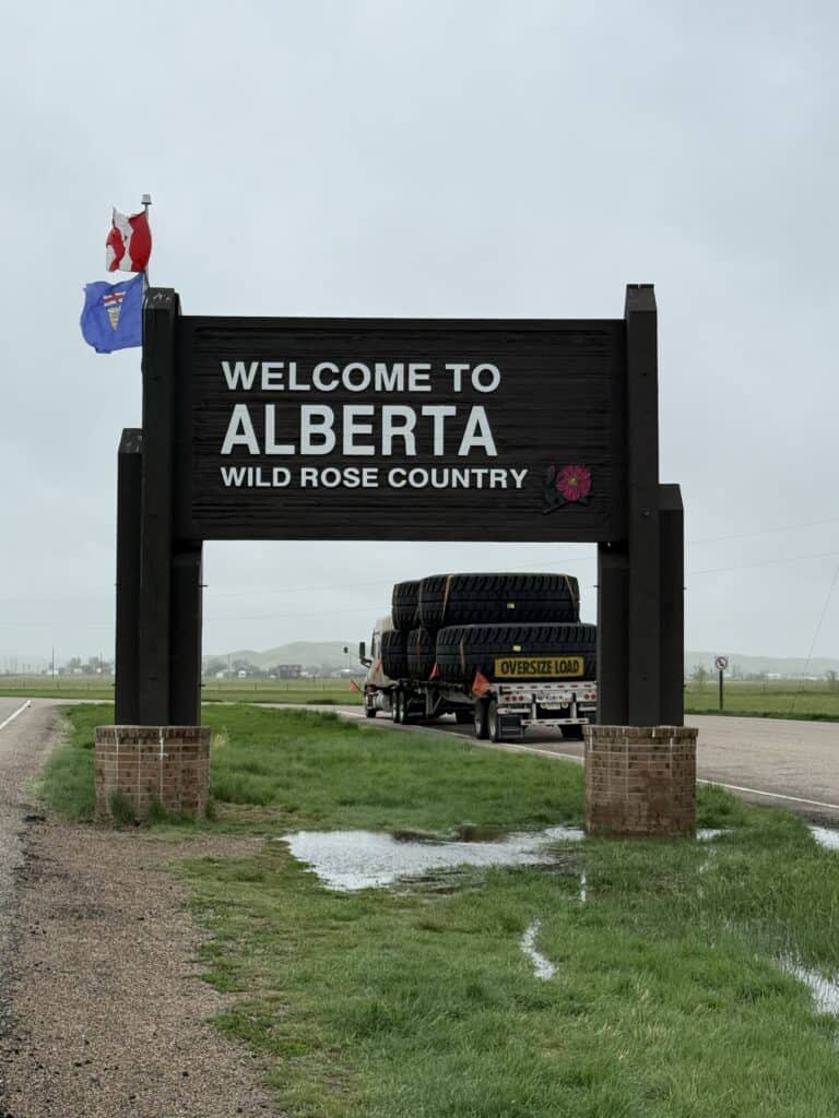 Welcome to Alberta Wild Rose Country sign at border with large transport truck behind.