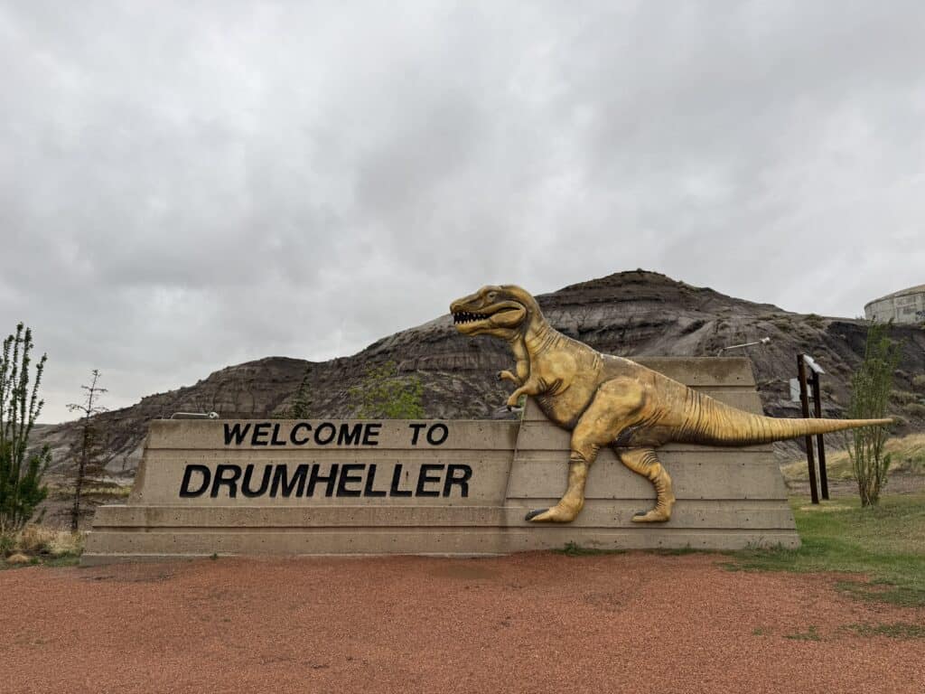 Welcome to Drumheller sign with dinosaur and hills in background on overcast day.