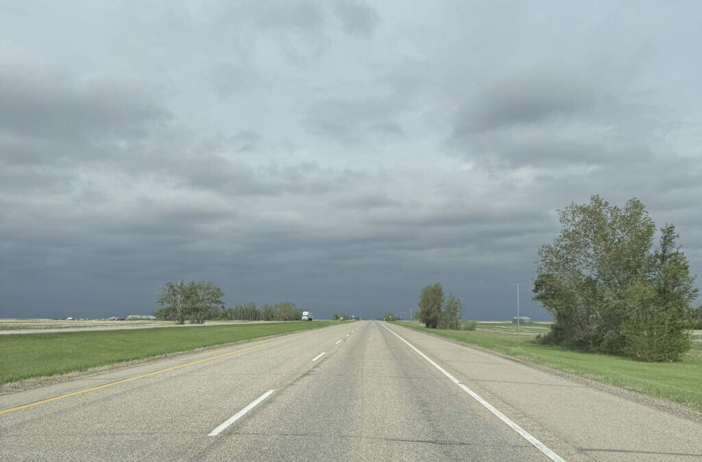 flat straight stretch of road through Canadian prairie on an overcast day.