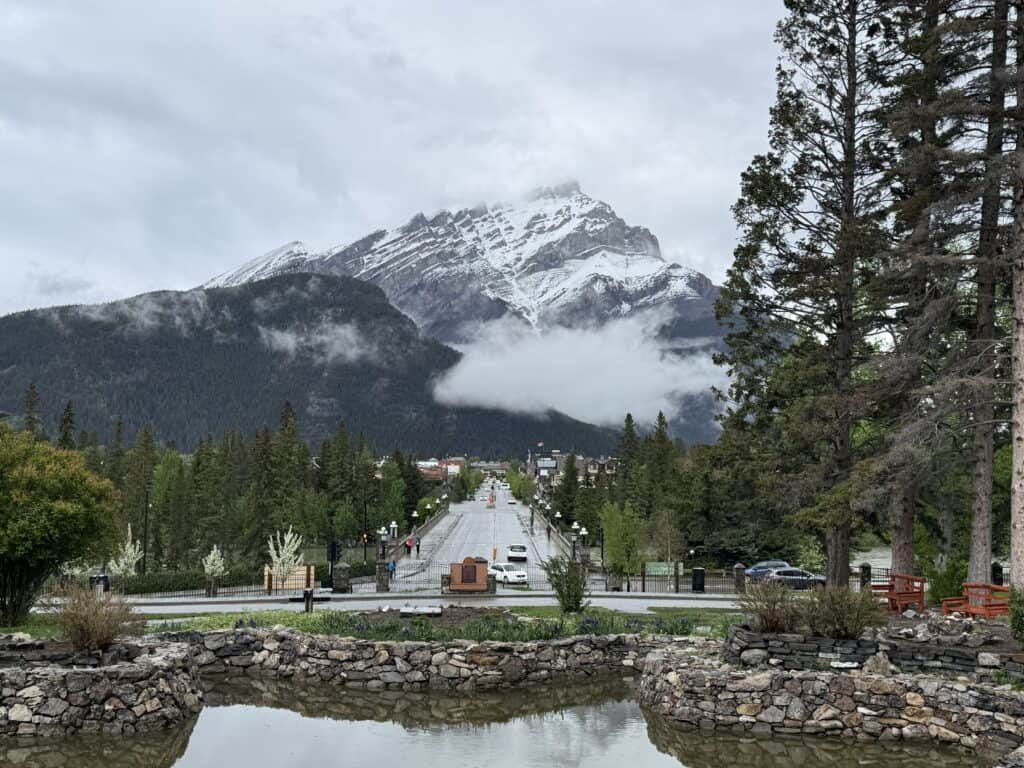 view of downtown Banff and snow capped mountains with low hanging white clouds from cascade gardens.
