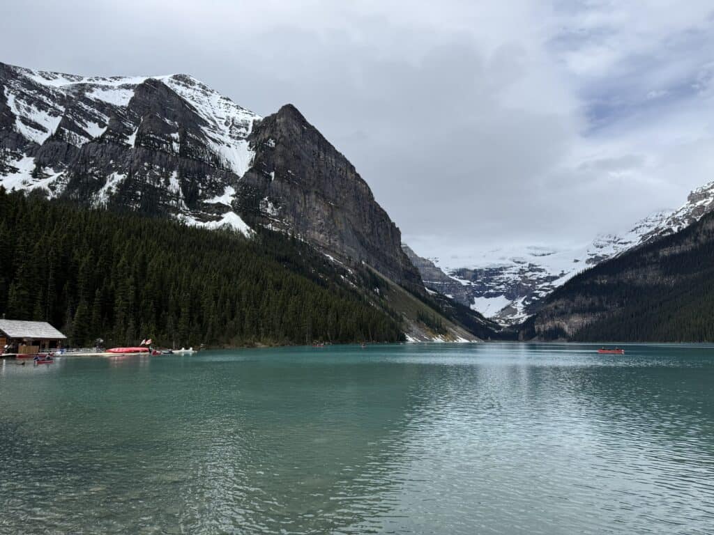 Lake Louise with snow-capped mountains and heavy clouds with just a hint of blue sky