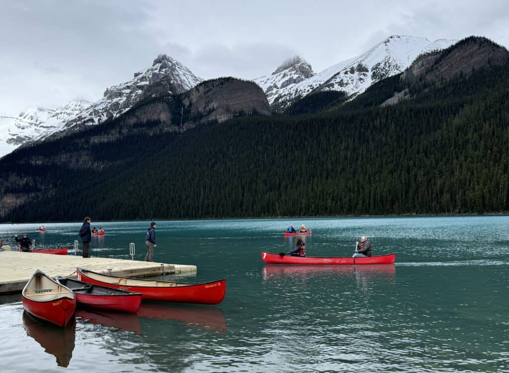 multiple red canoes near dock at Lake Louise with trees and snow-capped mountains in background.