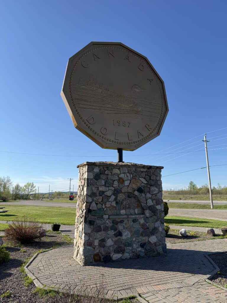 a large Canadian loonie dollar monument in Echo Bay, Ontario set against bright blue sky.