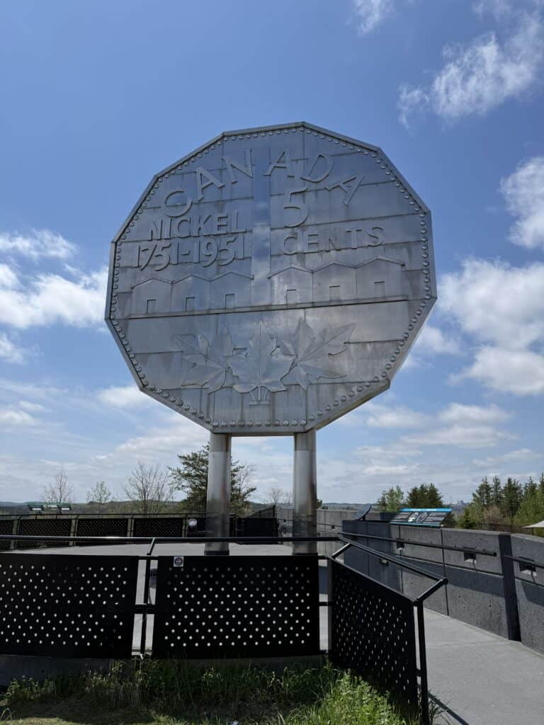 large Canadian nickel monument in Sudbury with bright blue sky and fluffy white clouds.