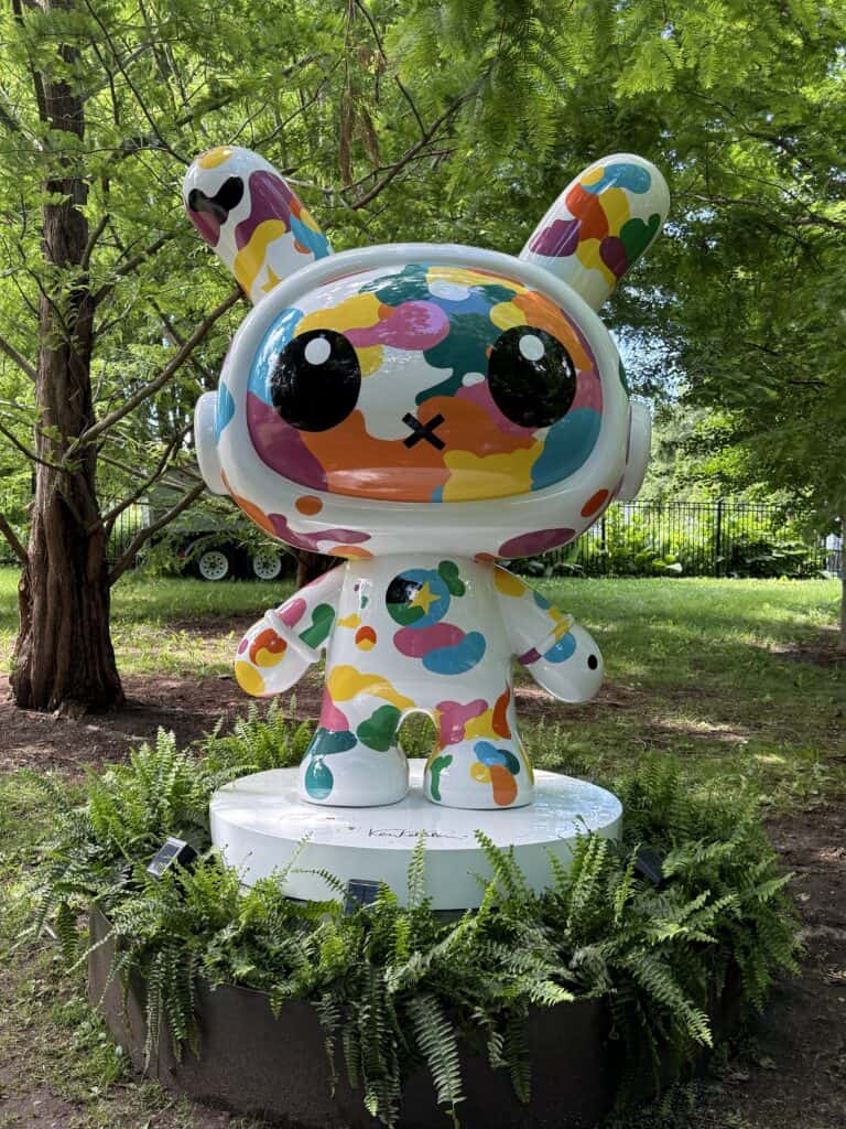multicoloured sculpture of Anchorball character - white background with blue, green, yellow, purple and orange splotches - with large round head.