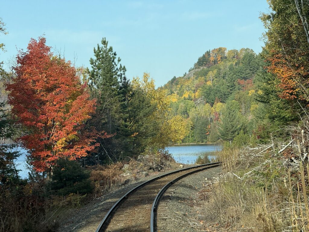 curved railway tracks with lake on the left and trees with fall colours.