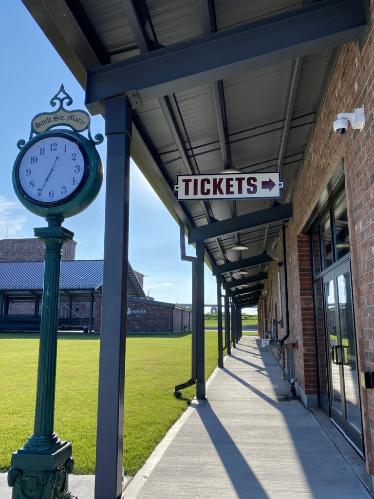 agawa canyon tour train office - walkway alongside of red brick building with old-fashioned clock and tickets sign.