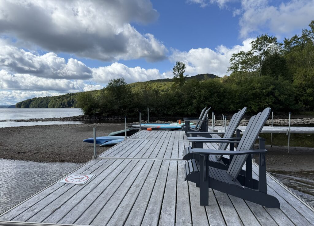 wooden chairs lined up on dock on lake massawippi with kayaks and woods in background.