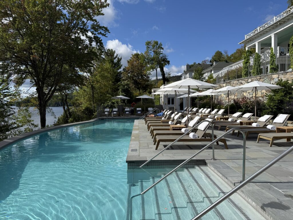 outdoor pool at manoir hovey with loungers and white umbrellas with lake visible in background.