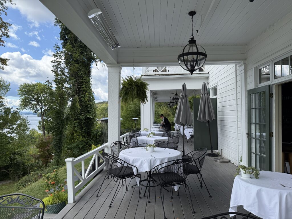 round tables with white tablecloths and black wrought iron chairs on verandah at Manoir Hovey.