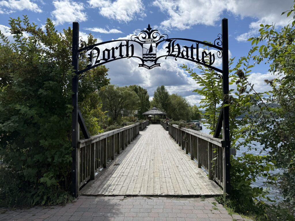 Wooden pedestrian bridge with North Hatley in black wrought iron overhead.
